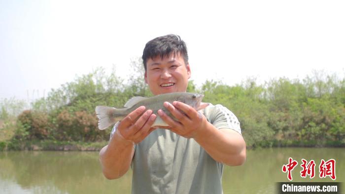 图为养殖户拿着鲈鱼笑呵呵地站在鱼塘边。　西平县委宣传部供图